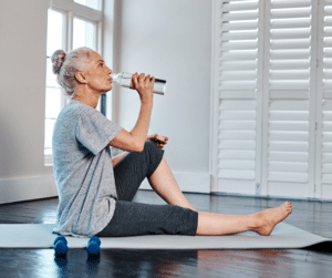 An older woman drinking water on a yoga mat